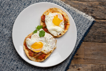 Fried eggs with sauce and tortilla called rancheros for  breakfast on wooden background. Mexican food