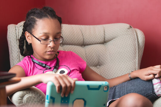 Portrait of a teenage girl with cornrows and glasses, sitting and using her electronic tablet device