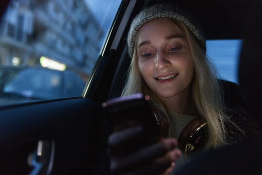 Smiling pretty woman reading smartphone in car