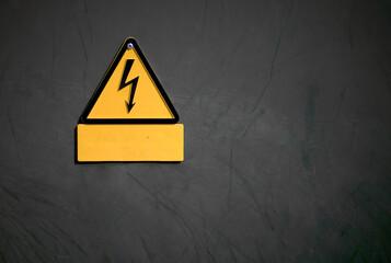 triangular yellow and orange high voltage danger sign on a dark,