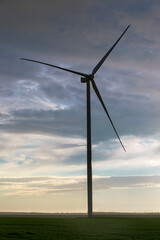 Obraz premium silhouette wind turbine offshore windmill made of iron with blades on field against a blue sky with clouds on sunset, alternative electricity preserving nature.