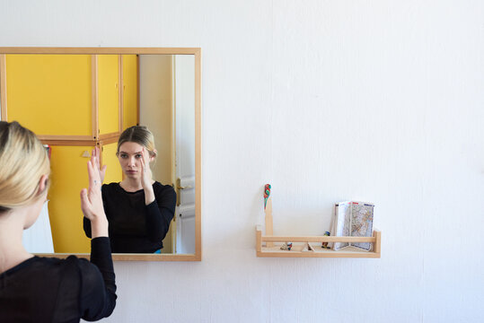 Woman holding hands close to her face and looking in the mirror.