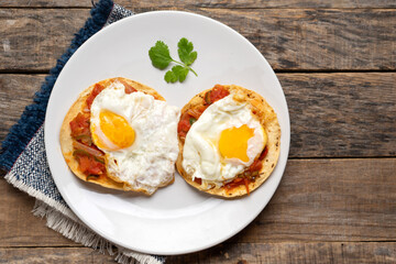 Fried eggs with sauce and tortilla called rancheros for  breakfast on wooden background. Mexican food
