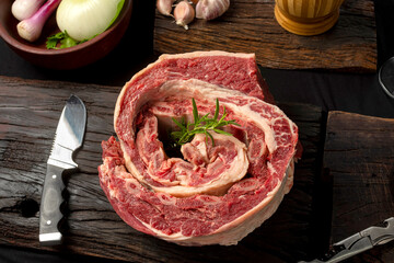 strip of roast beef, fresh beef ribs, on wooden board with vegetables and rotisserie knife with...