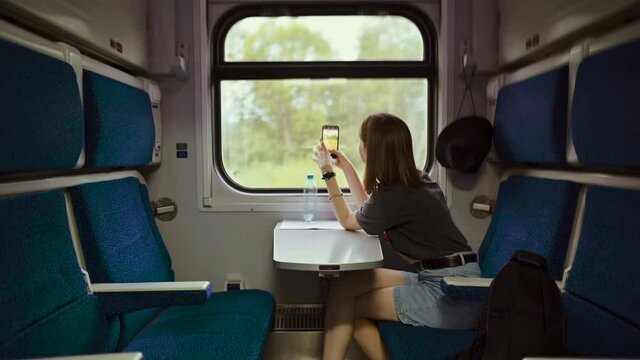 Woman rides in the compartment of a train car and uses the Internet on a smartphone with a smile on her face.