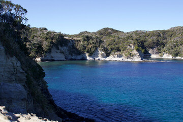 Katsuura Bay in Chiba Japan view, the ocean is a stunning deep blue color and the day is clear. It is a very idyllic scene. High cliffs and green hills.