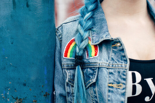 Closeup photo of jeans jacket of young girl with blue hair pigtails and rainbow lgbtq sticker on it. Showing independence and freedom