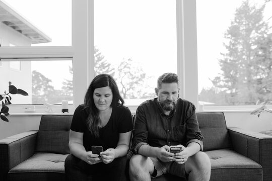 Unhappy couple at home on the couch on their phones