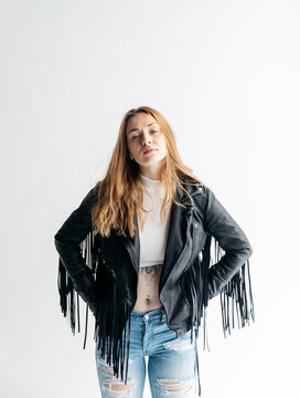 Portrait of Young woman in studio wearing leather jacket with fringe on white background.