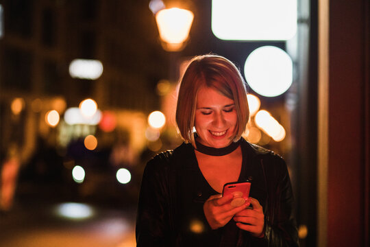 Blond woman with short hair using her smartphone on the street in the evening city.