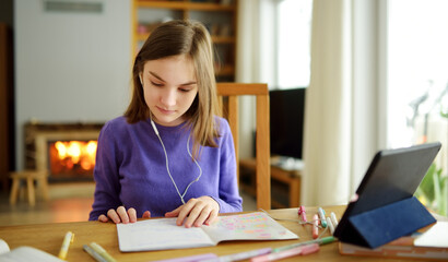 Fototapeta na wymiar Preteen schoolgirl doing her homework with digital tablet at home. Child using gadgets to study. Education and distance learning for kids. Homeschooling during quarantine.