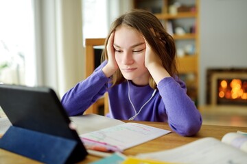 Preteen schoolgirl doing her homework with digital tablet at home. Child using gadgets to study. Education and distance learning for kids. Homeschooling during quarantine.