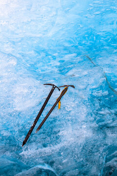 Two ice axes lying against blue ice of an iceberg