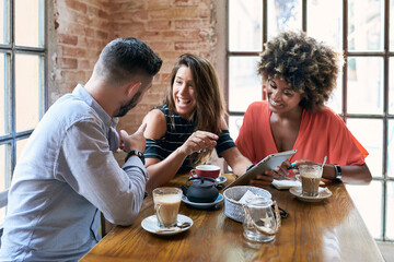 Portrait of laughing friends browsing tablet in cafe with drinks on table.