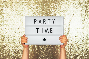 Woman holding lightbox saying party time against glittery background