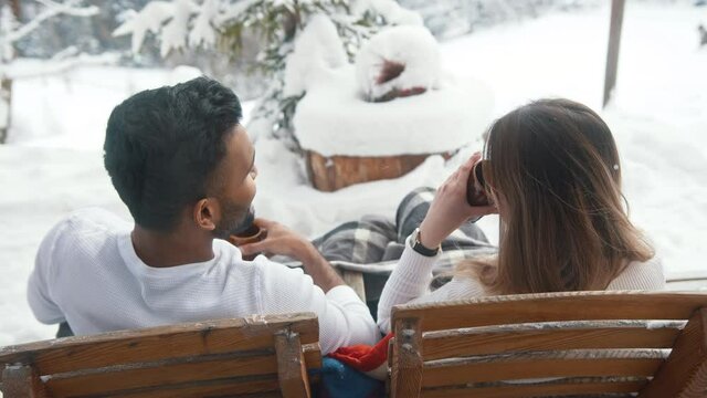 Back view. Happy young couple drinking hot chocolate while sitting on the bench outdoors on Valentines day. High quality 4k footage