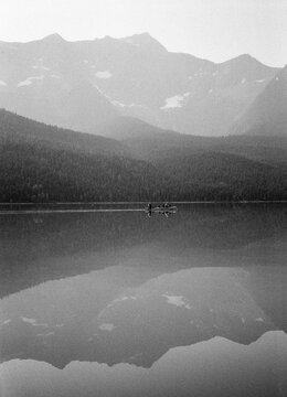 Two men canoeing across lake with perfectly still water for reflection BC Canada Bowron Lakes