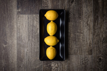 Fototapeta na wymiar Four lemons on a black plate on wood floor from above