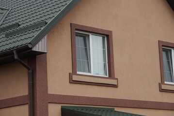 one white window on a brown wall of a private house under a green tiled roof 