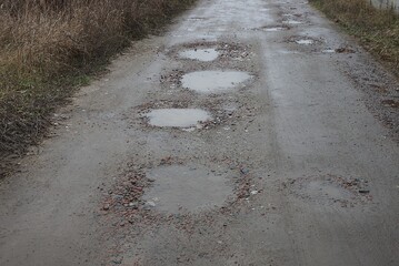 many pits and puddles with dirty water on the road from gray earth on the street