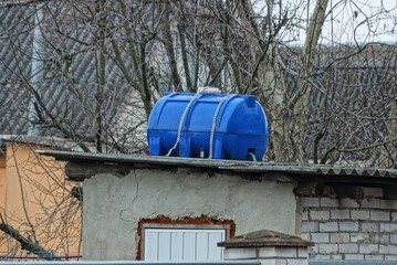one blue plastic barrel on the gray roof of a summer shower in a country yard