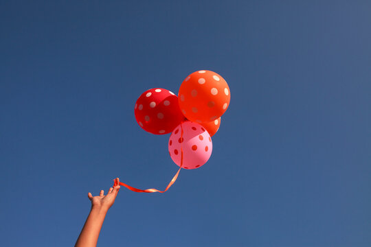 Girl holding colorful Balloons against blue sky