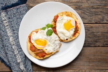 Fried eggs with sauce and tortilla called rancheros for  breakfast on wooden background. Mexican food