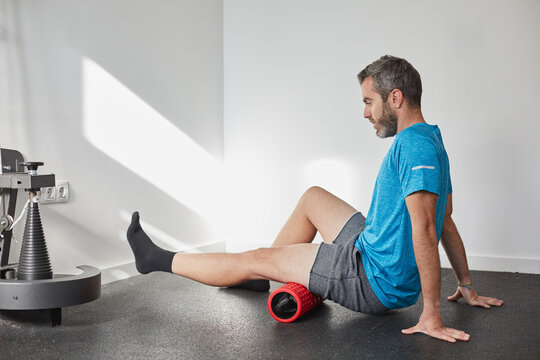 Male exercising the leg muscles with a roller foam in a fitness club