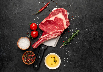Raw cowboy steak with spices on a knife on a stone background