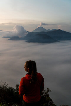 A young woman standing on the edge of a giant cliff, overlooking Mount Bromo and the Tengger Crater