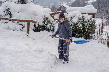 oy cleans the snow-covered paths near the house. Heavy snowfalls in winter. Changing weather conditions. Disaster. Large drifts of snow. The child helps to do the male work of cleaning the snow