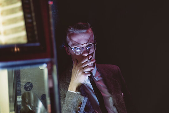 A dapper young man smokes and drinks by a jukebox