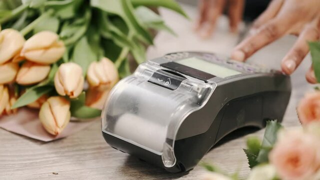 Cropped image of customer paying with credit card at flower shop, florist tying payment in terminal.