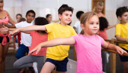 Fototapeta na wymiar Group of boys and girls training along ballet bar at dance class