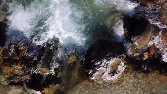 A top-down view of a small stream of clear mountain water that flows into a larger river. The stream of the most clear water
