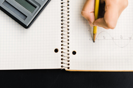 hand drawing trigonometry graph in notebook with calculator