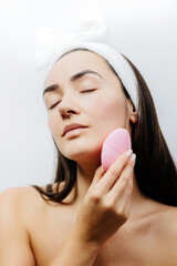 naked woman using cleansing brush for face deep cleaning . Beautiful woman clean face with...