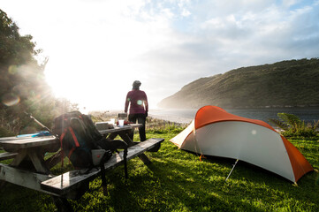 Rear view of a woman watching the sun set at a camp site on the Heaphy Track, Kahurangi National Park, New Zealand.