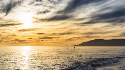 Obraz premium Sunset over the beach of Torre de Benagalbon, a coastal town of Andalucia in Spain, with 2 paddle boarder on the sea