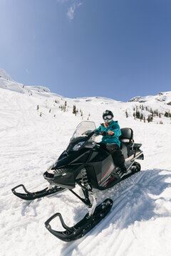 Young man sitting on a snowmobile on the snow on mountain landscape