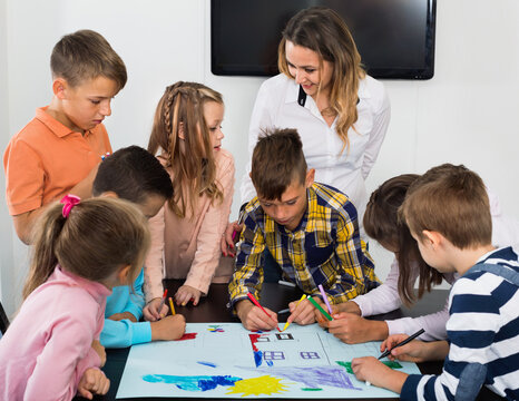 Happy smiling children with teacher drawing together in classroom