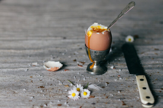 broken boiled egg in silver eggcup on wooden board