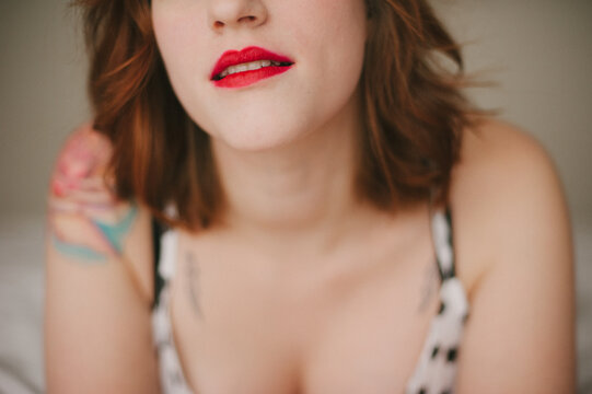 Young woman with flower tattoo lying on bed wearing bright red lipstick