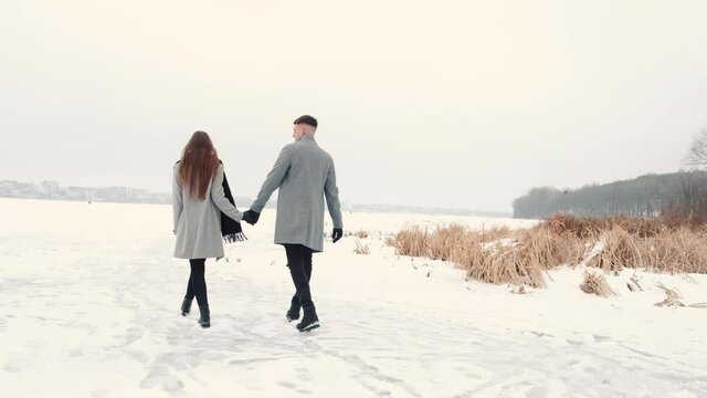 Young happy couple walking in winter near the lake and having fun on first snowfall. Winter, couple in love.