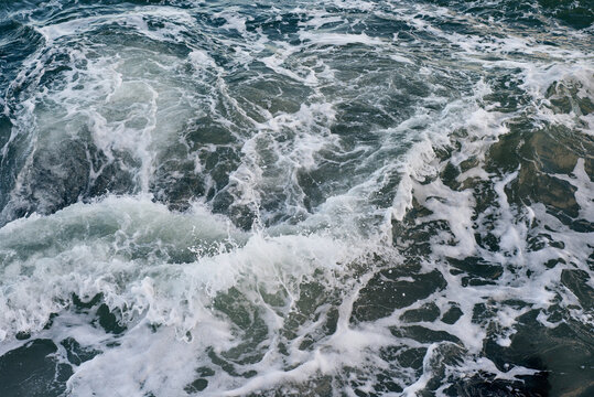 Waves breaking on underwater rocks, creating a small water vortex