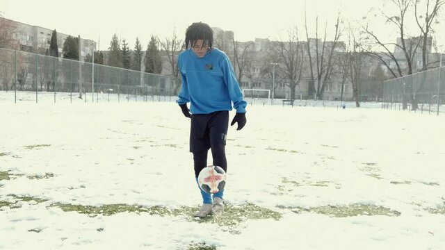 Outdoors activities. Young African american sporty man plaing football soccer at stadium in winter.
