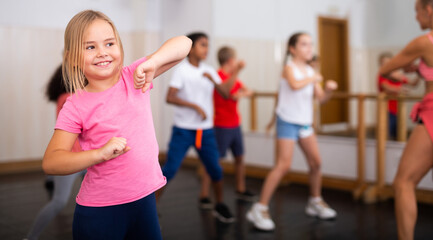 Portrait of cheerful preteen girl practicing dance movements with group of children in choreography...