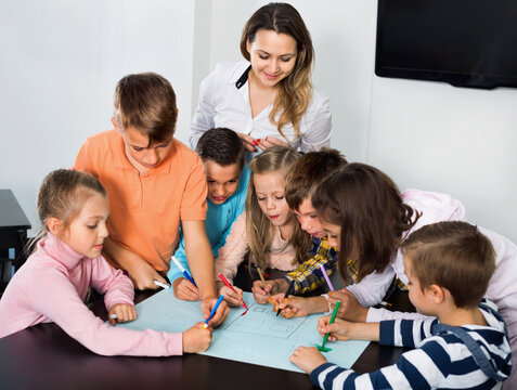 Little cute happy smiling children with teacher drawing together in classroom