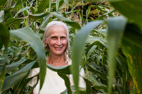 Elderly blonde woman with braids standing in corn field