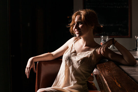 Red headed caucasian woman in lingerie sitting on dimly lit barstool